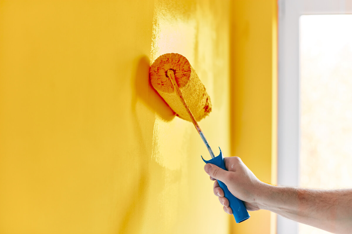 1- Paint roller with yellow paint against a wall